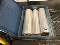 Three large rolls of clear commercial plastic wrap, 18 inches wide, placed inside a plastic container.