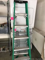 Full view of the green Werner ladder with four aluminum steps, showing general wear and store setting.
