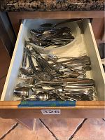 Pull-out drawer filled with mixed stainless steel flatware including knives, spoons, forks, and cocktail forks.