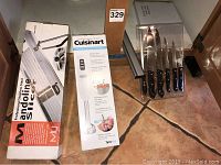 Setup showing boxed MIU stainless steel mandoline slicer and boxed Cuisinart hand blender, with knife set and magnetic knife holder displayed beside them on tiled floor.