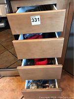 Four open drawers under kitchen counter, showing various kitchen items inside.