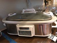Full view of Crockpot slow cooker showing glass lid, stainless steel body with white handles.