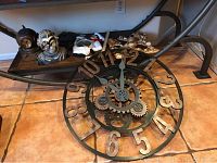 View of two large round gear-themed steampunk clocks on floor and steampunk robot head and shell barometer on shelf