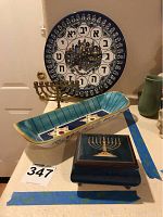 Clock featuring Jerusalem illustration with Hebrew letters around the perimeter, brass menorah, ceramic serving dish, and blue music box with menorah design visible