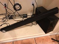 Samsung black soundbar lying horizontally on a floor with its cables visible, next to the subwoofer.