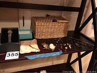 Overview photo showing Pulsar watch in box to left, yellow fabric pouch, blue fabric wristband, multiple brooches and pins, and beaded bracelet on shelf with woven basket behind.