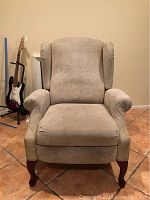 Front view of beige wing back reclining chair showing fabric upholstery and wooden legs.