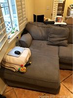 Gray sectional sofa in corner with chaise, pillows, and mouse on blanket.