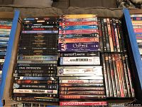Photo of a box containing multiple DVDs showing titles and cases lined up.