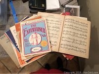 Photo showing a stack of sheet music booklets including 'The Entertainer' and an open booklet showing musical notation.