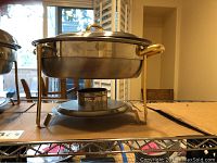 Oval Sunnex chafing dish on stand with lid and fuel holder beneath, showing gold-tone handles and normal wear.