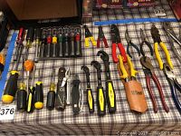 Photo showing an array of screwdrivers, socket drivers, pocket knives, and pliers with various colored handles including Wiss leather holster.