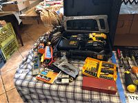 Wide view of the lot spread on a table including the DeWalt drill case, multiple testers, saws, levels, socket tools, and lock.