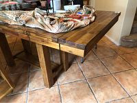 Photo showing corner of light oak high top dining table with drop leaves extended and items covered by cloth on top.
