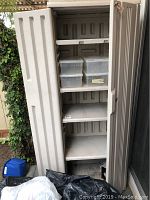Front view of a tall beige plastic storage cabinet with five shelves, the doors are open showing the inside including clear plastic storage boxes on one shelf.