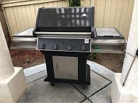 Full front view of Jenn Air outdoor grill showing stainless steel and black finish, side surfaces, hood, control knobs, and casters.