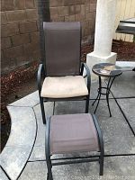 Full view of patio chair with cushion, footstool, and stone side table arranged on concrete patio with brick wall background.