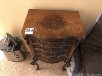 Front view of wood standing jewelry case showing carved drawer fronts and paw feet on legs.
