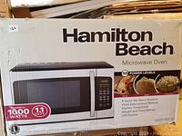 Packaging box front showing Hamilton Beach branding, microwave photo, 1000 watts power and 1.1 cu.ft. capacity.