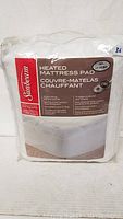 Packaged Sunbeam heated mattress pad in original clear plastic packaging showing front label with product details and brand.