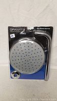 Front view of Gravitti rain shower head and curved arm in original packaging, sealed blister pack with black and blue background.
