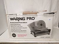Photo of the retail box of Waring Pro Professional Food Slicer showing product image and specifications, confirming it is a factory refurbished unit with genuine parts and warranty.