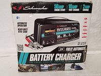 Front and side views of the Schumacher battery charger box showing product branding, amperage ratings, and device image.