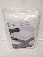 New Mainstays mattress pad in clear plastic packaging showing product label and partial mattress illustration.