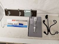 Photo of assorted clothes hanging hooks, including a brown metal hook rail with chrome hooks, white towel bar, white adhesive robe hook, and two black metal decorative hooks.