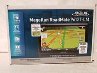 Box front view showing Magellan RoadMate 9612T-LM navigation device with highlighted features including 7-inch touchscreen, 3D landmarks, junction view, speed limit display, and traffic camera alerts.