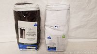Lot containing two packs of Mainstays grommet top window panels: one brown pack, one white pack with blue labels.