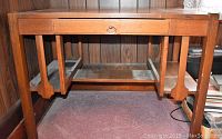 Front view showing full desk, drawer with metal ring pull, vertical slat leg design, and wood grain finish.