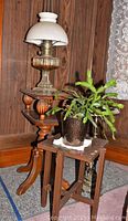 Full view of oil lamp, ashtray stand, planter table with plant, and side table in background
