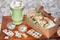 Photo of stereoscope viewer, box of picture cards, vase with stamps and bowls with stamps on wooden table