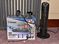 Swann Pro Security In a Box with four black outdoor cameras on and around the box; Sharper Image Ionic Breeze 3.0 air purifier in black tower design beside it