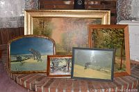 Photo showing all five framed art prints arranged together on a hearth with brick background. Prints depict wolves, forest, rural road, and cityscape scenes in various frame styles and sizes.