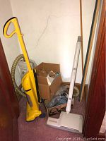 Wide shot showing yellow upright vacuum, white vacuum, boxes with attachments and hoses in corner