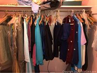 Wide view of ladies clothing on hangers, showing a variety of tops, sweaters, and pants in assorted colors.