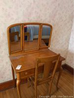 Full view of the vintage wooden vanity with tri-fold mirror and wooden chair in front.