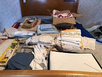 Full view of assorted embroidered linens, including pillowcases, tablecloths, and place settings in a variety of colors and lace accents, plus a pair of white satin gloves.