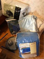 Overview photo showing packaging of 3 comforters, 2 pillows, and the Roomba vacuum cleaner on a hardwood floor.