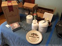 Overview of the lot showing Gevalia coffee maker box, ceramic canisters, clear glass Coca-Cola bottle, McDonald's glasses, strawberry pie plate and other glassware on blue table