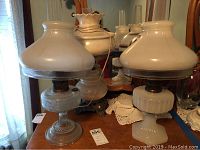 Two clear glass oil lamps with milk-glass shades on wooden dresser in front of mirror