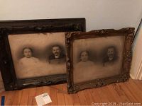 Two framed vintage black-and-white photographs leaning against a wall on a hardwood floor. Both frames show damage and wear.
