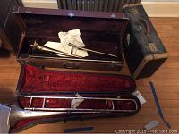 Overview of two trombones and their cases on hardwood floor.