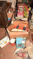 Wide view showing the lot of vintage toys including boxed items, toys in cardboard boxes, and an antique doll. Shows the overall collection and condition.