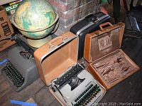 Wide angle photo showing three vintage typewriters and a globe. Smith Corona Classic 12 typewriter in brown case, Smith Corona Sterling in black case, Royal desk typewriter, vintage globe on stand.