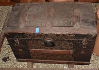 Front view of antique steamer trunk showing metal latch, decorative stamped leather panels, metal studs, and side handles