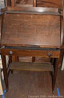 Full view of vintage wooden secretary desk from the front showing slant top and drawer below