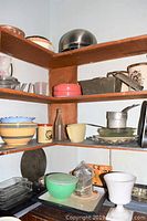 Corner shelf with stacked ceramic mixing bowls, small glass and ceramic bowls, enamelware canister tin, bottle, and various small kitchen items